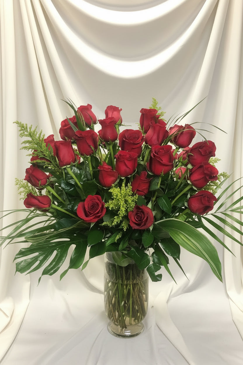 A bouquet of red roses arranged in a clear glass vase with green foliage and water visible at the base.