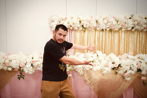 Man posing in front of a floral backdrop with decorative drapes