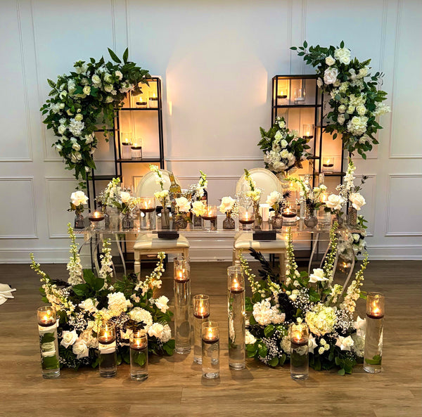 Decorative setup with floral arrangements and candles on a wooden floor.